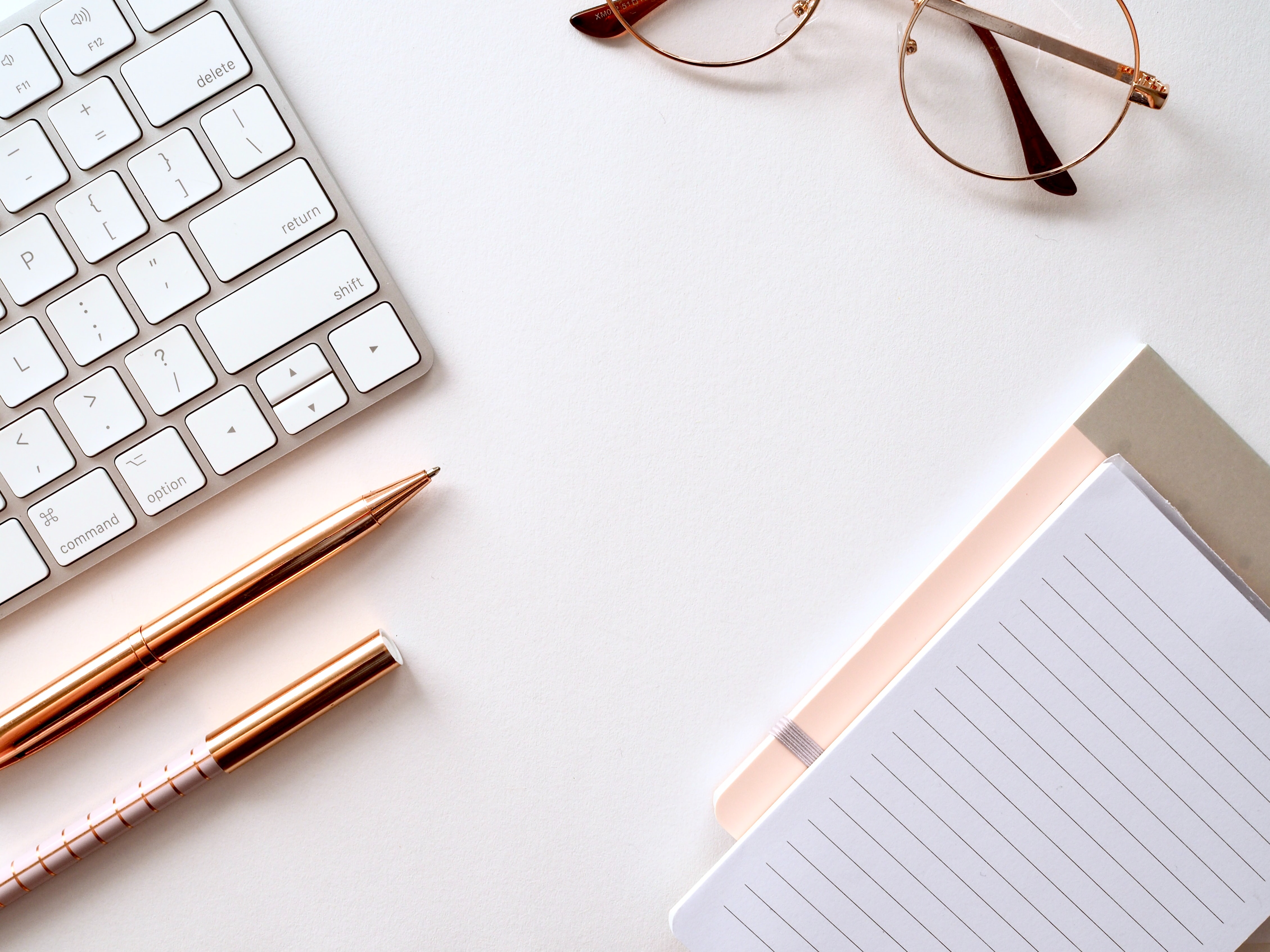 work desk with a keyboard, pen, glasses, and notebook